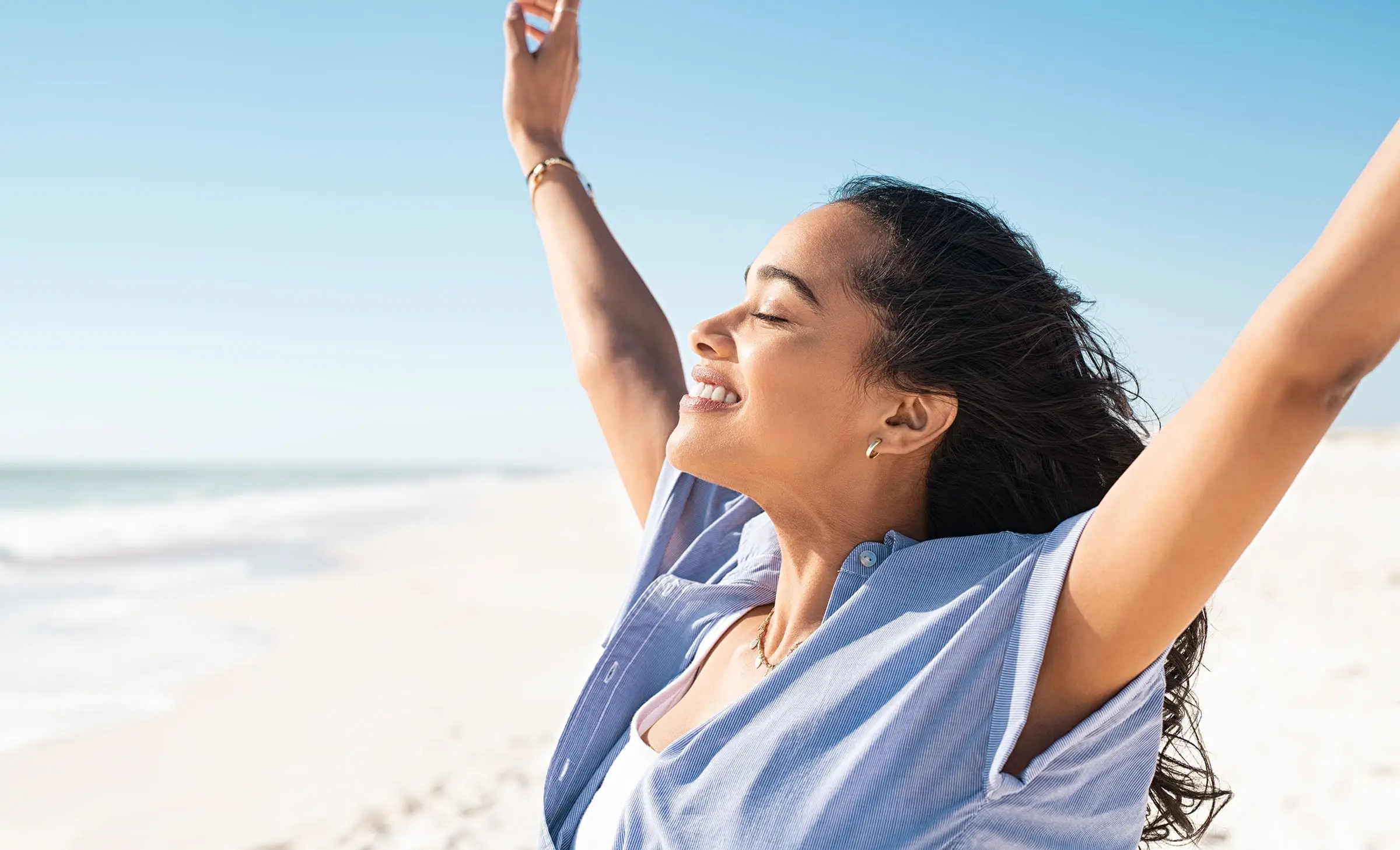 Happy woman standing on the beach and enjoy the sun tan with arms outstretched.