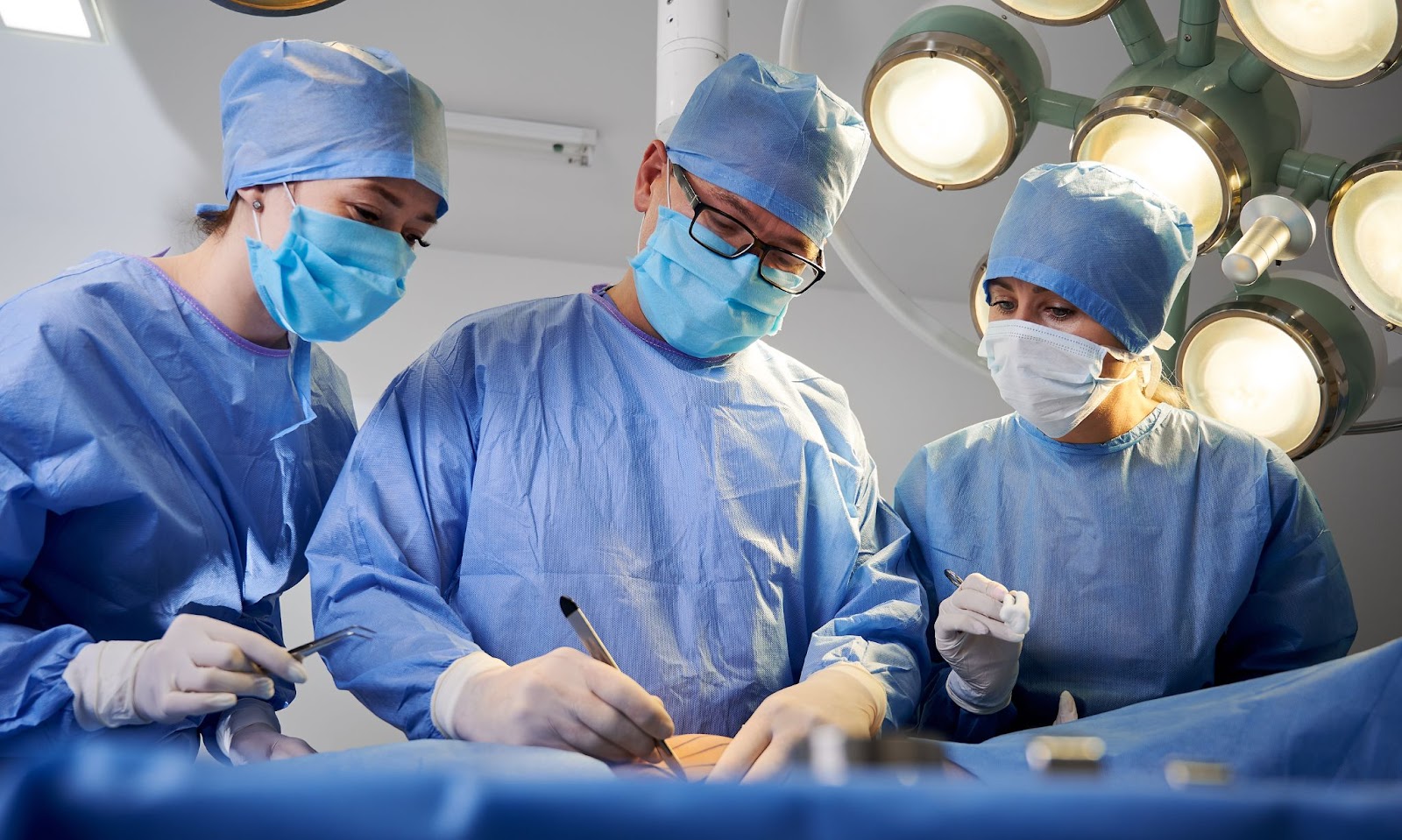 Team of surgeons operating on a patient for aesthetic tummy tuck surgery under surgical lights.