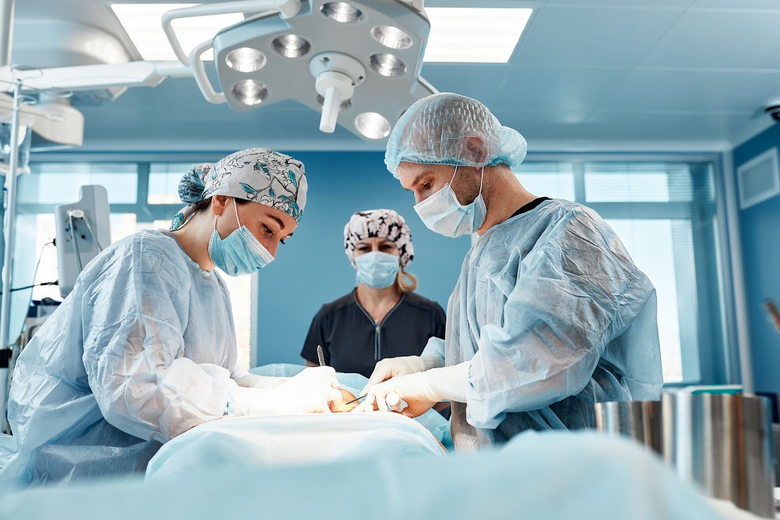 Team of surgeons operating on a patient for aesthetic tummy tuck surgery under surgical lights.